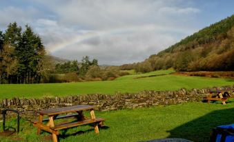 a picnic table is situated in a grassy field with a rainbow visible in the background at YHA Brecon Beacons Danywenallt