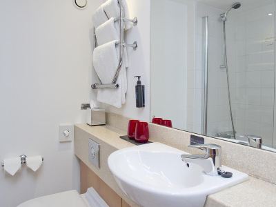 a modern bathroom with white walls , a mirror , and various toiletries on the counter , including soap dispensers and towels at Village Hotel Liverpool