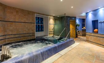 a large , blue - tiled indoor pool with jets and a marble floor , surrounded by wooden walls and lit by a yellow light at Dalhousie Castle Hotel