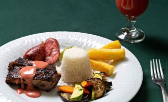 a plate of food with rice , meat , and vegetables is placed next to a glass of juice at Brotas Eco Hotel Fazenda