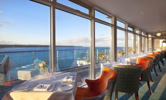 a dining room with a view of the ocean , featuring a dining table , chairs , and a television at Cliff House Hotel