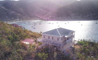 aerial view of a white house surrounded by mountains and a body of water , with boats in the water nearby at Ocean View Villas