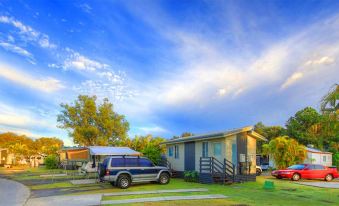 a blue van is parked in front of a house with a boat and trees surrounding it at Big4 Gold Coast Holiday Park