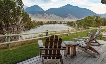 a wooden deck with two adirondack chairs , overlooking a river and mountains in the distance at Yellowstone Valley Lodge, Ascend Hotel Collection