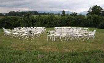 a large outdoor wedding ceremony with rows of white chairs arranged in an open field , surrounded by green grass and trees at Harmony Hill Bed & Breakfast