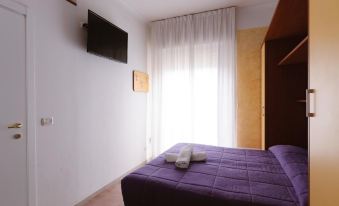 a cozy bedroom with a purple bed , white curtains , and a tv mounted on the wall at Hotel Viking