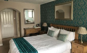 a large bed with a blue and white blanket is in a room with green patterned walls at The Anchorage Hotel