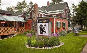 a sign for the inn is displayed in front of a red house with purple flowers at The Inn