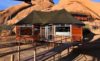 a tent is set up in a desert - like area with a wooden deck and large rock formations in the background at Spitzkoppen Lodge