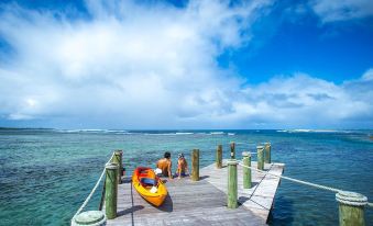 a man in an orange life jacket is sitting in a kayak on a wooden pier , surrounded by clear blue water at Sinalei Reef Resort & Spa