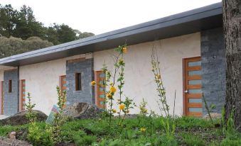 a house with a stone wall and wooden door , surrounded by greenery and flowers , under a clear sky at Hampton Halfway Hotel Motel