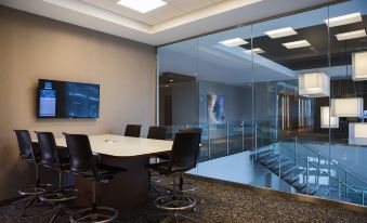 a conference room with a large table , black chairs , and a glass wall separating the room from the auditorium at AC Hotel Cincinnati at Liberty Center