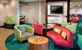a modern lounge area with colorful chairs , a wooden coffee table , and a tv mounted on the wall at SpringHill Suites Philadelphia Willow Grove
