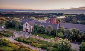 aerial view of a large house surrounded by trees and a body of water , with the sun setting in the background at Rosewood Cape Kidnappers