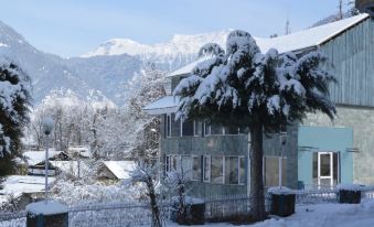 a snow - covered house with a large tree in the front yard , surrounded by snow - covered mountains at WoodStock Hotel