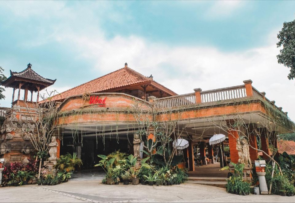 a brick building with a curved roof and large windows , surrounded by green plants and trees at Ubud Hotel & Cottages