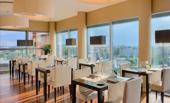 a dining room with white chairs and tables , a large window overlooking the city , and some chairs on a dark wood floor at NH Padova