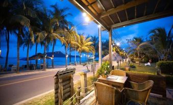 a beautiful beach scene with palm trees , a wooden porch , and a table set for dinner at Dolphin Bay Beach Resort