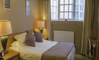 a well - lit bedroom with a large window , white bed linens , and beige curtains , along with a lamp on the nightstand at The Kings Head Hotel