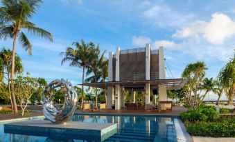 a modern building with a large pool and a sculpture in front of it , surrounded by palm trees at Pullman Maldives All-Inclusive Resort