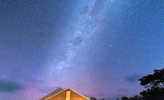 a wooden building with a blue sky filled with stars and the milky way above at Ratho Farm