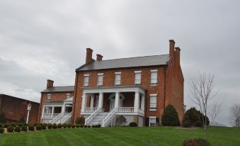 a large brick house with a gray roof and white columns is surrounded by green grass at General Morgan Inn
