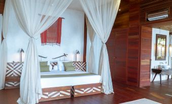 a bed with a white canopy is situated in a room with wooden floors and red and white curtains at Moro Ma Doto