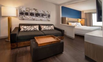 a modern living room with a couch , coffee table , and a bed in the background at SpringHill Suites Herndon Reston