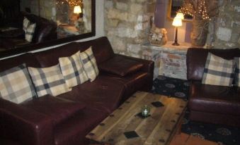 a cozy living room with a brown leather couch and a wooden coffee table , surrounded by chairs at George Inn