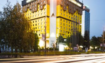 a large yellow building surrounded by trees and traffic on the street , with a building in the background at Hotel Holiday