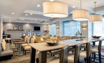 a modern hotel lobby with a dining area featuring tables , chairs , and large windows that offer views of the city at Hampton Inn Hallandale Beach-Aventura