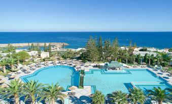 a large resort pool surrounded by palm trees , with the ocean visible in the background at Iberostar Selection Creta Marine