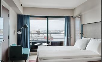 a modern hotel room with a large window offering a view of the city , a comfortable bed , and a green chair at Radisson Blu Caledonien Hotel, Kristiansand