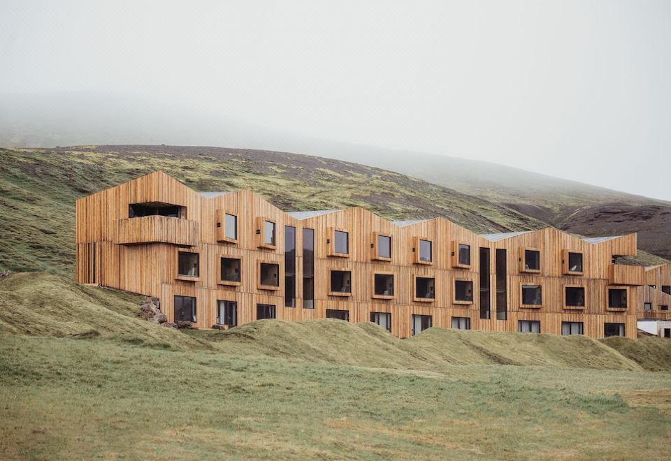 a large wooden building with multiple floors and balconies is nestled in a grassy field at Highland Base Kerlingarfjoll