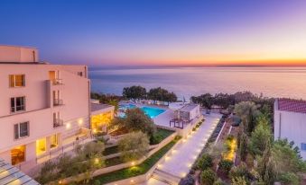 a large hotel with a swimming pool surrounded by trees and overlooking the ocean at dusk at La Luna Hotel - All Inclusive