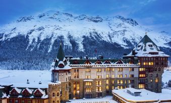 a large hotel surrounded by snow - covered mountains , with a lake in the background , creating a serene and picturesque winter scene at Badrutt's Palace Hotel St Moritz