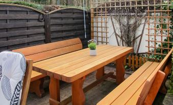 a wooden table and bench set with a small potted plant on the bench , surrounded by a fence and greenery at Karli