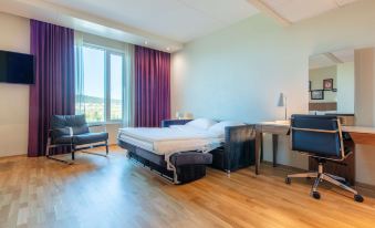 a modern hotel room with a large bed , couch , and desk , along with purple curtains and wooden flooring at Radisson Blu Hotel and Conference Cente, Oslo Alna