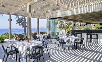 a restaurant with white tablecloths and black chairs is shown with a view of the ocean at White Rocks Hotel Kefalonia