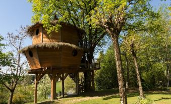 a tree house with a thatched roof is nestled among the trees in a grassy area at Auberge la Tomette, the Originals Relais