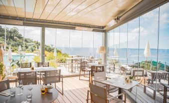 a restaurant with wooden tables and chairs , a view of the ocean through the windows at Hotel la Villa Douce
