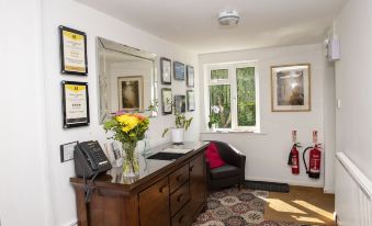 a well - decorated living room with various items , including a vase of flowers , a fire extinguisher , and a framed certificate on the wall at Bridleways Guesthouse & Holiday Homes