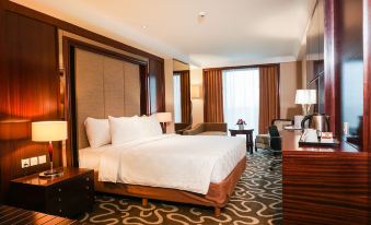 a large bed with white linens is in a room with a desk , chair , and lamps at Swiss-Belhotel Serpong