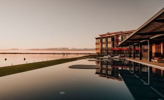 a large , modern building with a swimming pool in front of it , set against a backdrop of a lake and a sunset at The Sebel Yarrawonga Silverwoods
