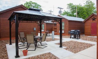 a patio area with a barbecue grill , dining table , chairs , and a pergola covered in a black metal frame at Texas Star Lodges