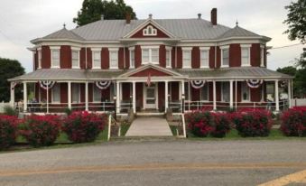 a large red and white house with a porch and porch railing , surrounded by greenery at Grand Victorian Inn