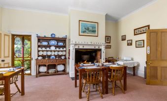 a dining room with a wooden dining table , chairs , and a fireplace in the background at Cambridge House Breakfast & Bed