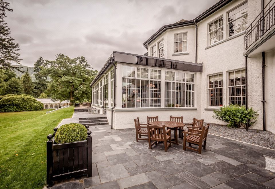 a large white building with a patio area featuring a dining table and chairs , surrounded by greenery at Dunkeld House Hotel