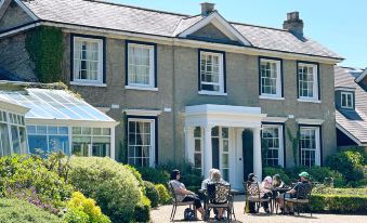a group of people are sitting outside in front of a large house , enjoying each other 's company at Park Farm Hotel