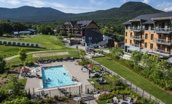 a large swimming pool is surrounded by grass and trees , with a resort visible in the background at Jay Peak Resort